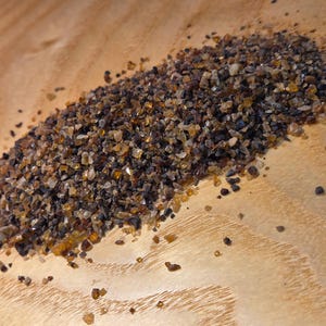 May include: A pile of small, irregularly shaped, amber and dark brown gemstones. The gemstones are scattered on a light brown wooden surface, with the light reflecting off the facets of the stones. The overall appearance suggests a collection of raw, natural crystals.