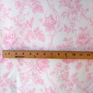 Pink floral toile fabric laid flat with a wooden Westcott ruler measuring twelve inches across the pattern.