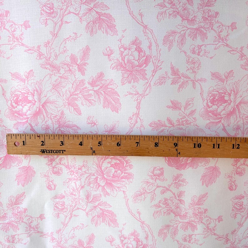 Pink floral toile fabric laid flat with a wooden Westcott ruler measuring twelve inches across the pattern.