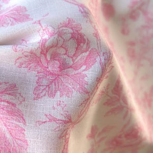 Close-up of textured fabric showing a folded section with pink floral toile print on white.