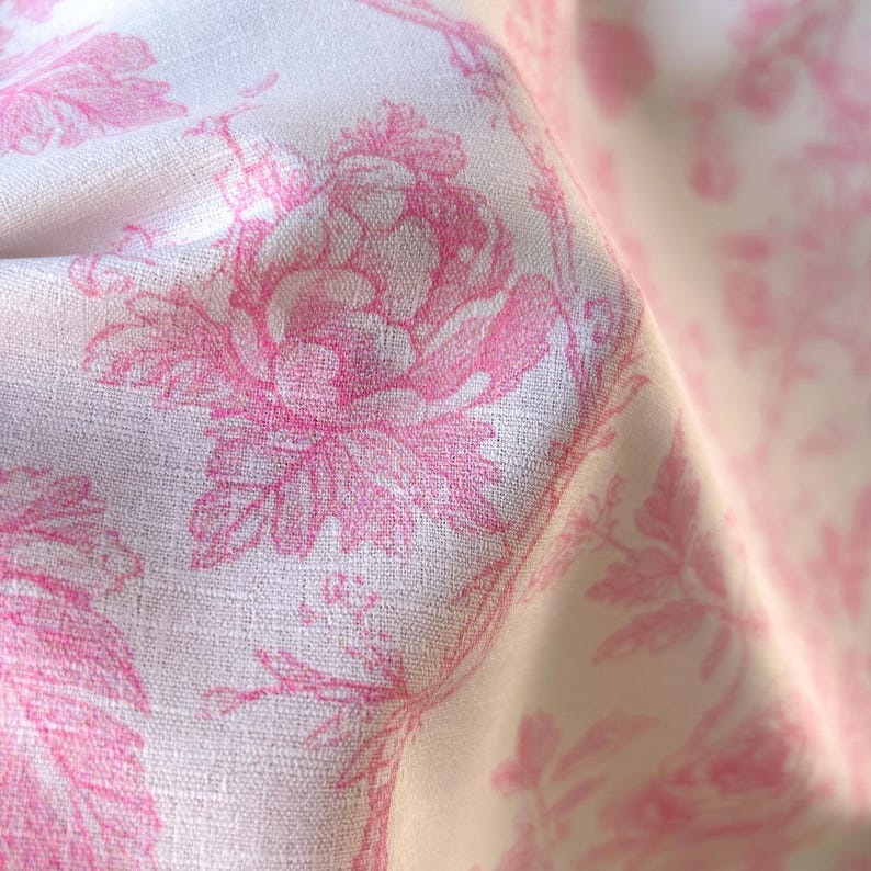 Close-up of textured fabric showing a folded section with pink floral toile print on white.