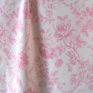 Pink and white toile de jouy fabric hanging in gentle folds with a repeating floral pattern.