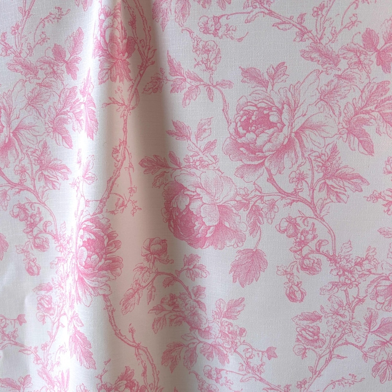 Pink and white toile de jouy fabric hanging in gentle folds with a repeating floral pattern.