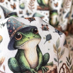 A close-up of a green frog in a wizard hat from the fabric pattern, with a blurred background of the same pattern.