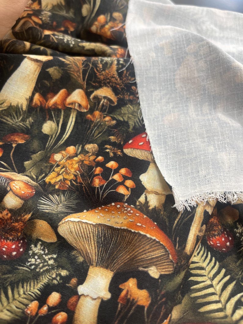 Dark woodland mushroom fabric shown next to a piece of plain white woven fabric.