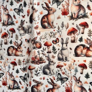 A close-up of folded fabric showing a pattern of rabbits, mushrooms, butterflies, and autumn leaves.