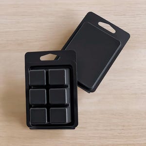 May include: Two black plastic packaging containers for wax melts. One container has six square compartments for wax melts. The other container is empty.