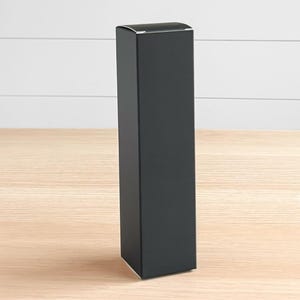 May include: A tall, rectangular black box with a slightly curved top. The box is standing upright on a light-colored wooden surface, with a white-painted horizontal plank background.