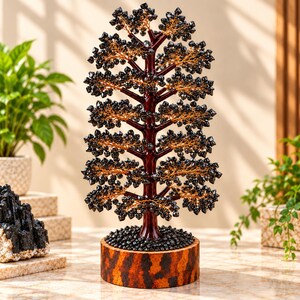 Puede incluir: Una escultura de árbol decorativa con un tronco y ramas de color rojo oscuro adornados con numerosas piedras pequeñas de color negro facetado similares a cristales. El árbol está montado sobre una base redonda con patrón moteado.