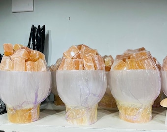 Op de afbeelding: Een verzameling decoratieve kristallen paddenstoelsculpturen. Elke paddenstoel heeft een witte basis en een top die bestaat uit oranje kristalbrokken. De paddenstoelen zijn op een witte plank geplaatst.