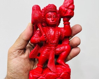 May include: A vibrant red statue of a deity, possibly Hanuman, holding a mace and a mountain. The figure is intricately detailed, with a crown and ornate clothing. The statue is on a small base, and the overall design is symbolic.