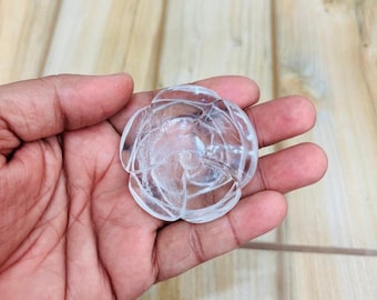 May include: A clear, rose-shaped crystal carving. The crystal is held in a hand, showcasing its intricate details and translucent quality. The carving is a decorative item.