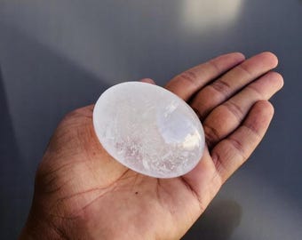 May include: A white selenite palm stone with a smooth, polished surface. The stone has a translucent appearance with visible internal striations.