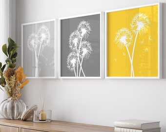 Puede incluir: Tres impresiones enmarcadas de siluetas de dientes de león sobre un fondo amarillo, gris y blanco. Las impresiones están colgadas en una pared blanca sobre un armario de madera.