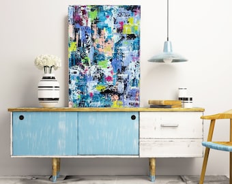 May include: Abstract painting with bright colors and geometric shapes, hanging above a blue and white dresser with a white vase and flowers.