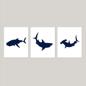 May include: Three navy blue silhouette prints of sharks on a white background. The prints feature a hammerhead shark, a great white shark, and a whale shark.