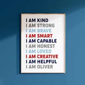 May include: A white framed print with the text "I AM KIND", "I AM STRONG", "I AM BRAVE", "I AM SMART", "I AM CAPABLE", "I AM HONEST", "I AM LOVED", "I AM CREATIVE", "I AM HELPFUL", and "I AM OLIVER" in different colors.