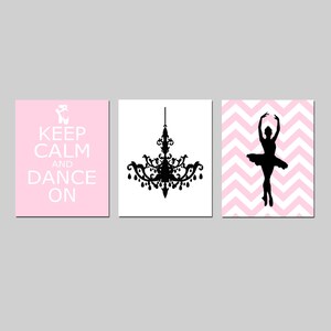 Op de afbeelding: Drie roze en witte ingelijste prints met zwarte silhouetten. De eerste print zegt "Keep Calm and Dance On". De tweede print toont een kroonluchter. De derde print toont een ballerina op een roze en witte chevron achtergrond.