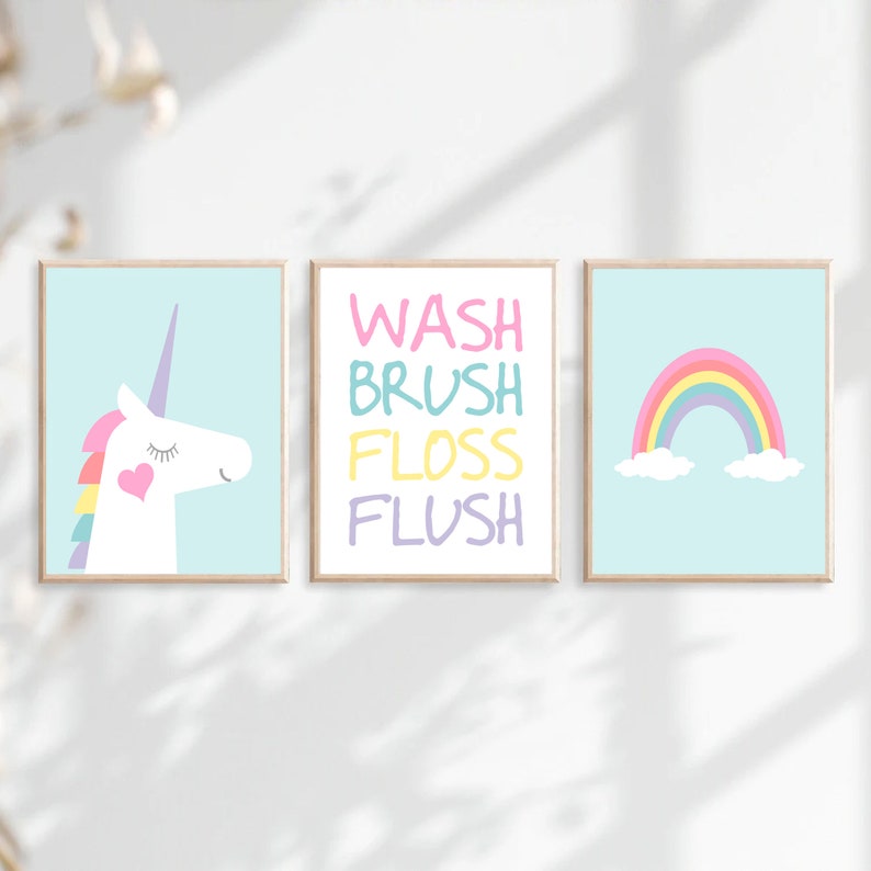 May include: Three framed prints with a pastel color scheme. The left print features a white unicorn with a rainbow mane and a pink heart on its chest. The middle print has the words "WASH BRUSH FLOSS FLUSH" in different pastel colors. The right print features a rainbow with clouds on a light blue background.