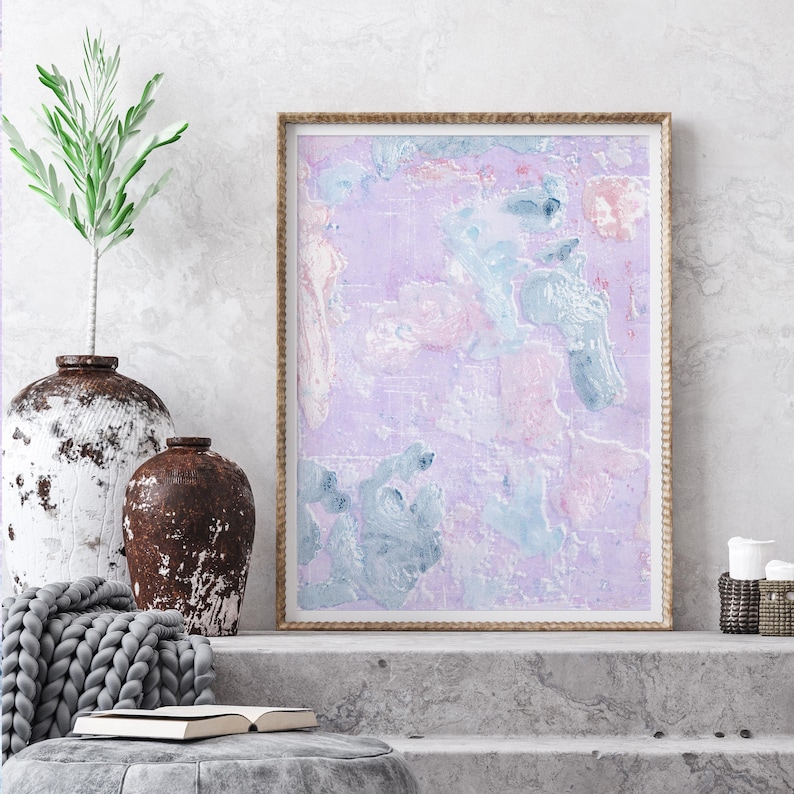May include: A framed abstract painting with a light purple background and blue and pink brushstrokes. The painting is displayed on a shelf with a gray knitted throw and two rustic vases.