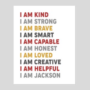 May include: A white background with the text "I AM" in red, gray, gold, and black. The text includes the words "KIND, STRONG, BRAVE, SMART, CAPABLE, HONEST, LOVED, CREATIVE, HELPFUL, JACKSON".