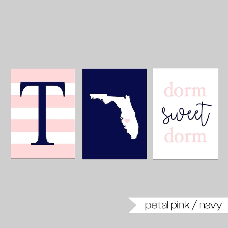 Puede incluir: Tres impresiones art&iacute;sticas de pared en rosa p&eacute;talo y azul marino. Una impresi&oacute;n presenta una letra "T" azul marino sobre rayas rosas y blancas. Otra muestra el contorno blanco de Florida sobre azul marino. La tercera dice "dorm sweet dorm".