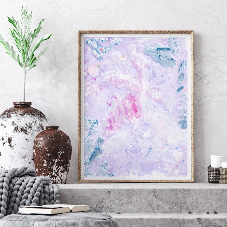 May include: Abstract painting in a light purple, pink, and blue color scheme. The painting is framed in a natural wood frame and is displayed on a concrete shelf.