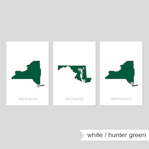 May include: Three white prints with green outlines of the states of New York, Maryland, and New York. Each print has a small gray heart marking a city: Brooklyn, Baltimore, and Bronxville.
