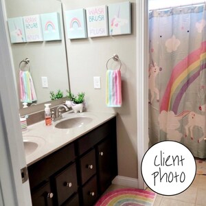 May include: A bathroom with a double vanity sink, a rainbow shower curtain with unicorns, and a rainbow rug. The walls are decorated with framed prints that say "Wash Brush Flush" and feature rainbows and unicorns.