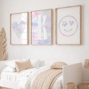 May include: Three framed prints with pastel watercolor designs. The first print features a heart shape with a rainbow pattern. The second print features the letter K with a rainbow pattern. The third print features a smiley face with a rainbow pattern and a heart for one eye.