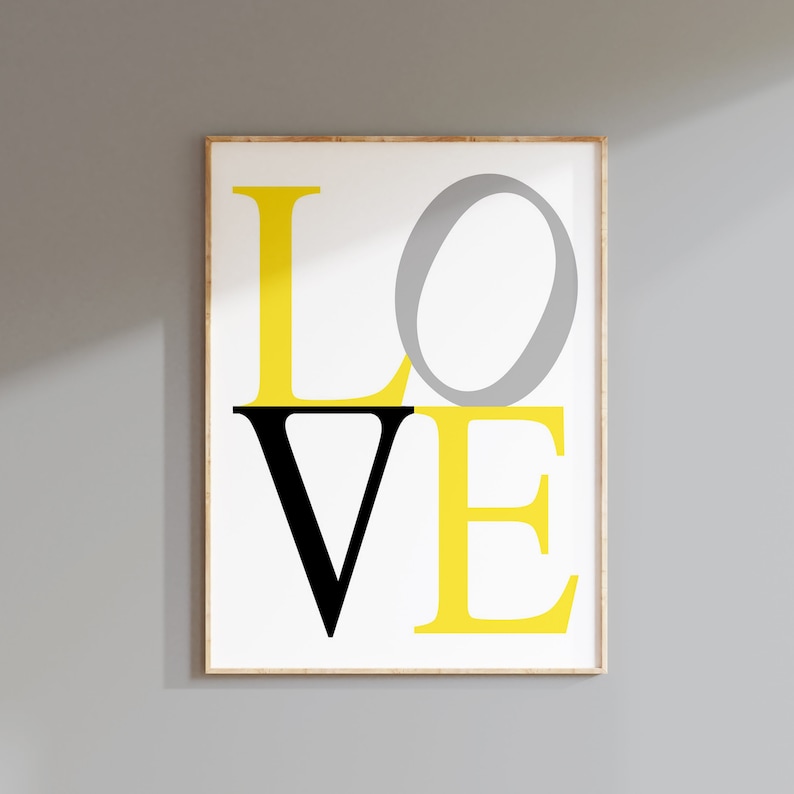 May include: A framed print with the word 'LOVE' in yellow, black, and gray letters. The letters are stacked on top of each other, with the 'O' in gray and the 'V' in black. The background is white.