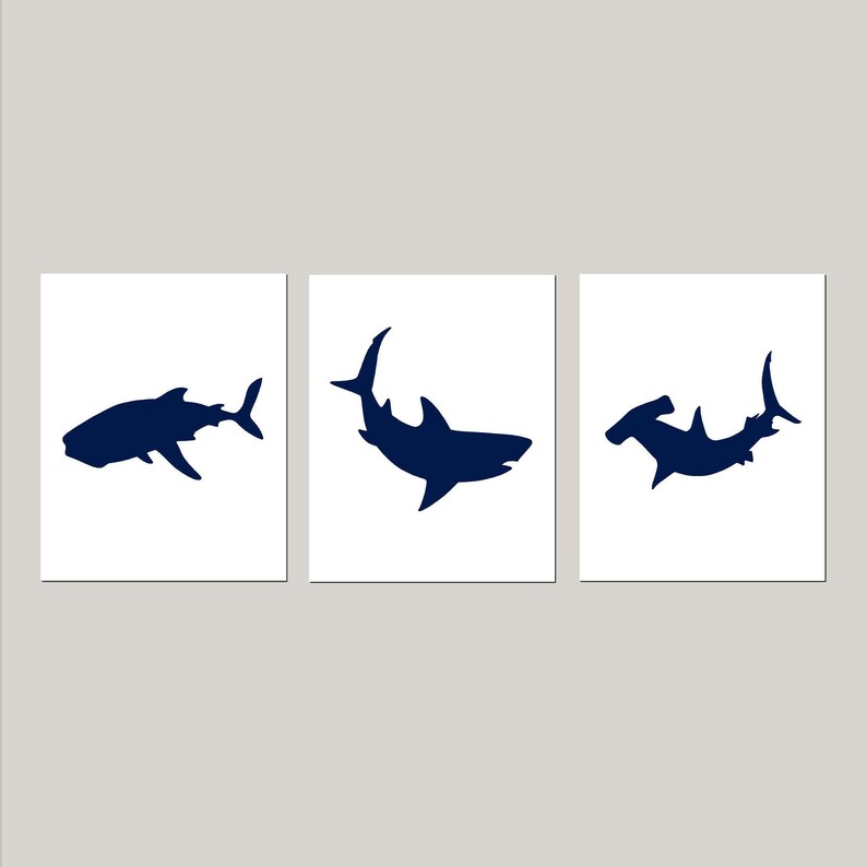May include: Three navy blue silhouette prints of sharks on a white background. The prints feature a hammerhead shark, a great white shark, and a whale shark.