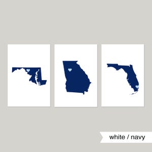 May include: Three white prints with navy blue outlines of the states of Maryland, Georgia, and Florida. Each state has a small light blue heart in the center.