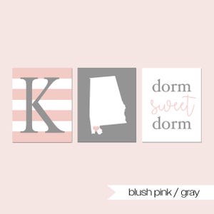 Puede incluir: Tres impresiones de arte mural cuadradas en rosa rubor y gris. Una presenta una letra "K" gris sobre rayas rosas y blancas. Otra muestra el contorno blanco de Alabama sobre un fondo gris. La tercera dice "dorm sweet dorm".