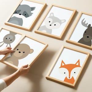 May include: Six framed prints with different animal illustrations. The prints are in a light wood frame and feature a fox, a raccoon, a bunny, a bear, a wolf, and a moose. The prints are all in a minimalist style with simple lines and colors.