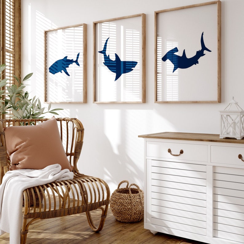 May include: Three framed prints of blue shark silhouettes on a white wall. The prints are in wooden frames with white mats. The frames are hanging above a white cabinet with a wooden top.