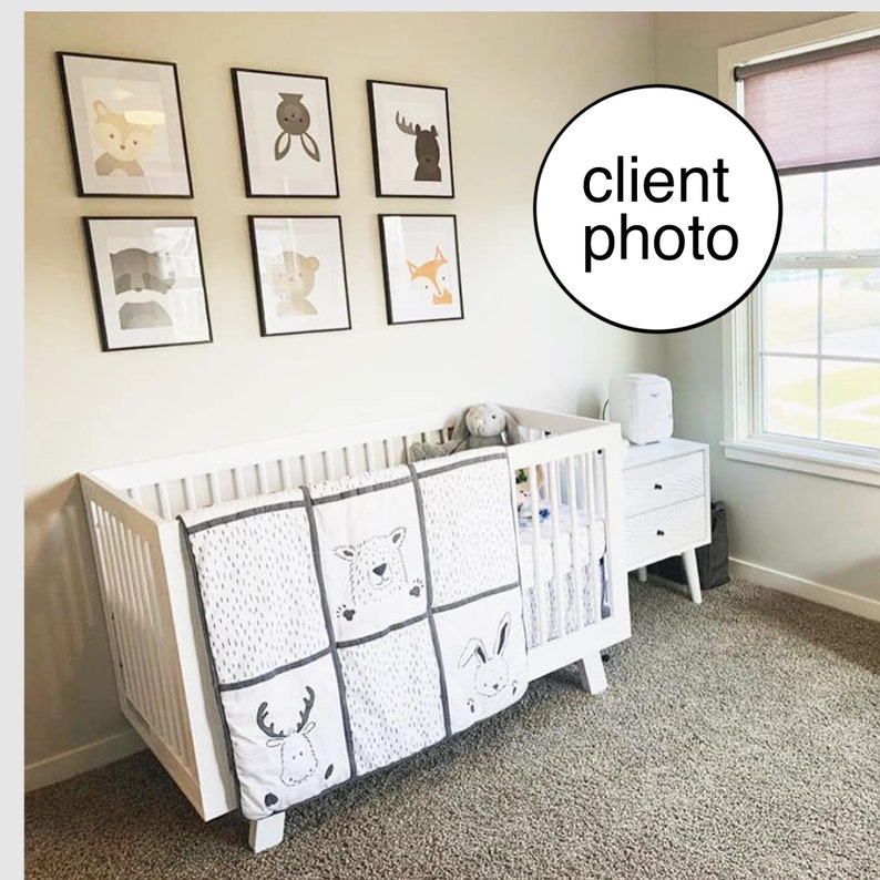May include: White crib with a white and gray animal print quilt. The crib is in a nursery with a white wall and framed animal prints.