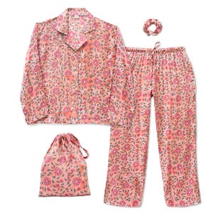 以下が含まれることがあります： ボタン付きシャツ、ドローストリングパンツ、シュシュ、お揃いの巾着袋を含む、花柄のピーチ色のパジャマセット。 花柄のデザインは、ピンクの花と緑の葉が特徴です。