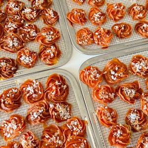 May include: Close-up of several trays of dried fruit arranged in a spiral shape. The fruit is a vibrant orange colour and is sprinkled with white sugar crystals.