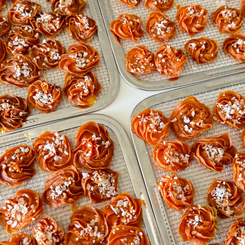 May include: Close-up of several trays of dried fruit arranged in a spiral shape. The fruit is a vibrant orange colour and is sprinkled with white sugar crystals.