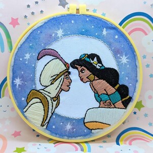 May include: Embroidered hoop art featuring Aladdin and Jasmine from Disney's Aladdin. The characters are depicted in a romantic pose against a blue starry night background.