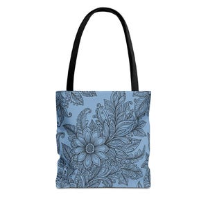 Könnte beinhalten: Eine Tragetasche mit hellblauem Hintergrund und einem grauen Blumenmuster. Die Tasche hat schwarze Griffe und eine große Blume in der Mitte des Designs. Das Blumenmuster umfasst Blätter und andere botanische Elemente.