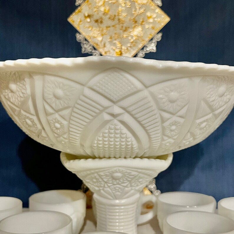May include: A white milk glass punch bowl with a pedestal base and matching cups. The bowl has a raised, intricate design.