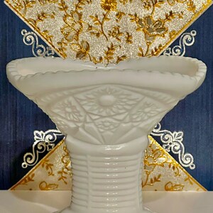 May include: White milk glass pedestal bowl with a scalloped rim and a floral design. The bowl is on a pedestal with a ribbed design.
