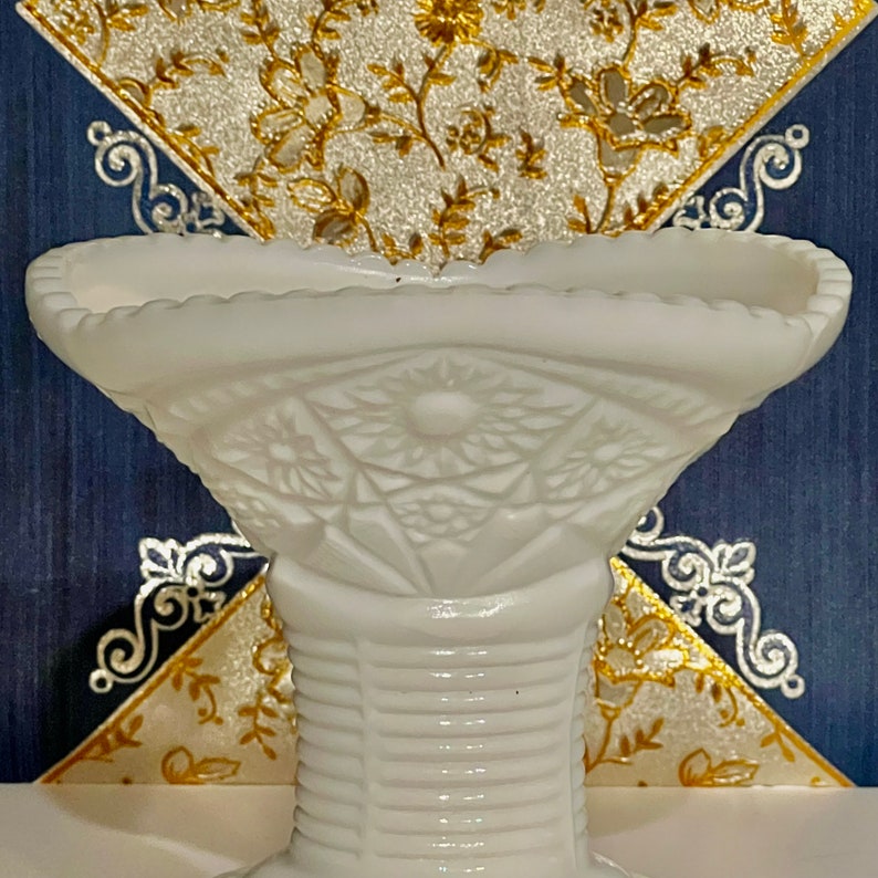 May include: White milk glass pedestal bowl with a scalloped rim and a floral design. The bowl is on a pedestal with a ribbed design.