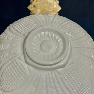 May include: White milk glass bowl with a raised, intricate design. The bowl has a scalloped edge and a center design that resembles a sunburst.