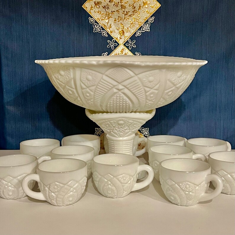 May include: A white milk glass punch bowl set with a pedestal base and 12 cups. The bowl and cups have a raised, embossed design.