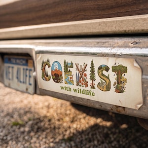 May include: A rectangular bumper sticker featuring the word COEXIST in stylized letters filled with nature scenes including mountains, a bear, a river, a deer, an owl, a squirrel, a wolf, and trees, with the text with wildlife below it.