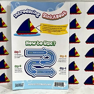 K&ouml;nnte beinhalten: Eine Packung SinkABoat-Spielzeugboote mit Anweisungen. Die Boote haben blaue Segel, gelbe und rote Akzente. Die Packung enth&auml;lt den Text "Introducing SinkABoat" und "How to Use?"