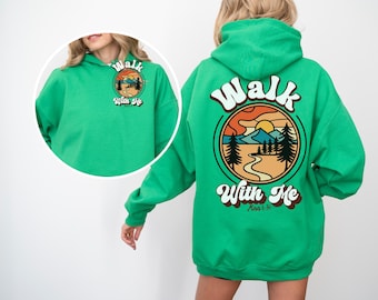 Könnte beinhalten: Grüner Kapuzenpullover mit Grafik auf Vorder- und Rückseite. Die Grafik auf der Rückseite zeigt eine Berglandschaft mit den Worten "Walk With Me". Die Grafik auf der Vorderseite ist eine kleinere Version des Designs auf der Rückseite.